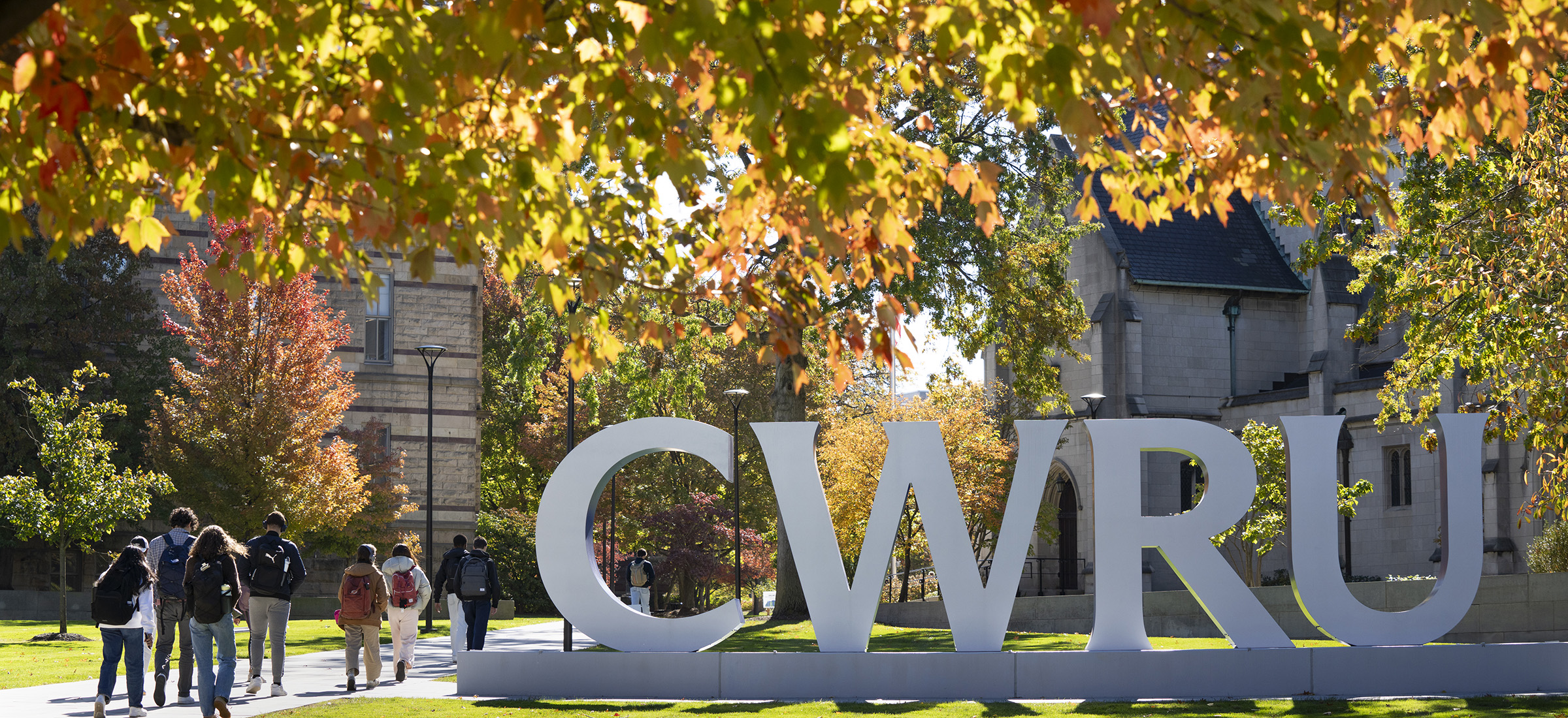 Students walk on the Binary Walkway past giant CWRU letters in the fall